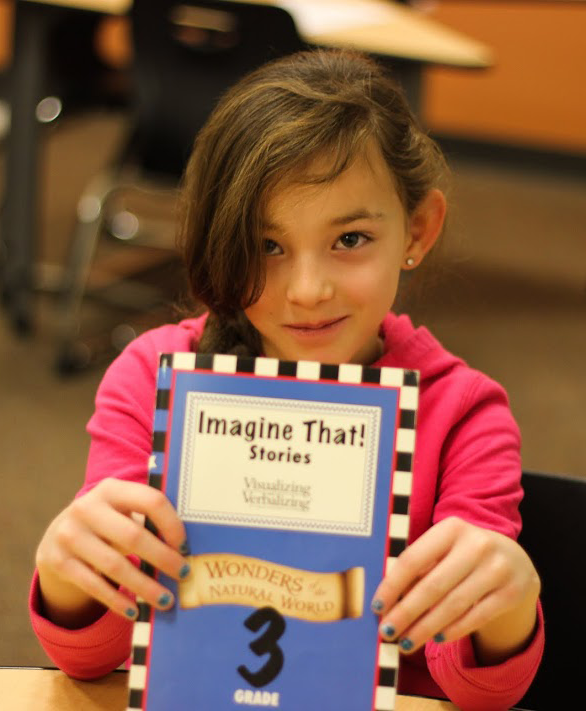 A young student holding up an Imagine That! Stories book - Wonders of the natural world