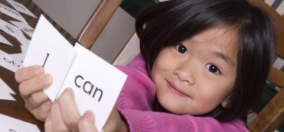 A happy student holding up 2 flashcards that say "I" and "Can"